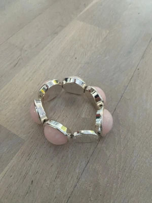 Rosa pärlarmband från SONS OF SWEDEN - Snyggt armband med stora, ljusrosa pärlor infattade i silverfärgade metallramar. Märkt SONS OF SWEDEN på baksidan. Armbandet har en rund form och elastisk tråd som gör det enkelt att ta på och av.