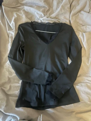 Svart långärmad topp med spets - Svart långärmad topp med v-ringning och spetsdetaljer vid halsringningen och ärmsluten. Tunn och mjuk, perfekt att styla lager på lager eller bära som den är. Enkel men ändå elegant design.