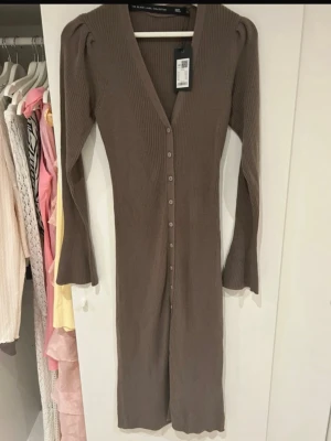 Brun stickad långklänning - Snygg brun stickad långklänning med v-ringning och långa ärmar. Aldrig använd 