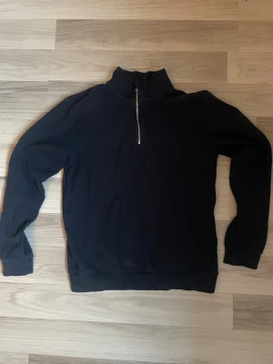 Mörkblå half-zip tröja - En stilren mörkblå hoodie med half-zip dragkedja framtill och hög krage. Passar folk som är runt 160-170cm lång. Tillverkad i mjukt sweatshirtmaterial som känns skönt mot huden. Perfekt för en avslappnad och trendig look. Långa ärmar och ribbade muddar vid ärmslut och nederkant. Tröjan har inga större skador och är i hyfsat bra kvalitet.