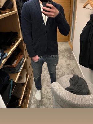 Cardigan tröja - Snygg mörkblå kofta med sjalkrage och stora knappar framtill. Två praktiska fickor framtill. Perfekt att slänga över en t-shirt för en chill men stilren look.