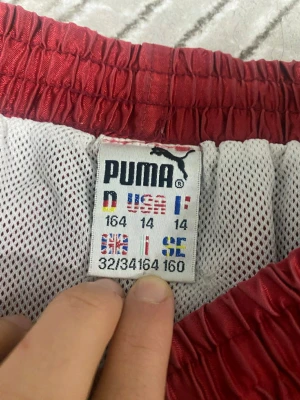 Röda shorts från Puma med snörning - Snygga röda shorts från Puma med vit snörning i midjan och meshfoder på insidan. Shortsen har en sportig look och elastisk midja för skön passform. Perfekta för sommarens alla aktiviteter.