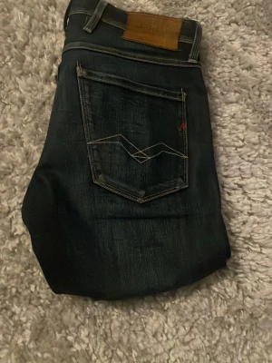 Mörkblå jeans från replay - Säljer ett par mörkblå jeans från replay med klassisk femficksmodell och snygga kontrastsömmar på bakfickorna. Jeansen har en rak passform och är tillverkade i slitstark denim. Perfekta för dig som gillar stilrena och tidlösa jeans.