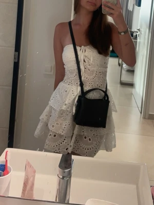 Vit kort klänning med spets och volang - Söt vit kort klänning med broderade spetsdetaljer och volanger. Klänningen är ärmlös, har snörning framtill och omlottkänsla i kjolen. Perfekt för sommarens alla tillfällen. Är köpt i Grekland därför vet jag inte märket.