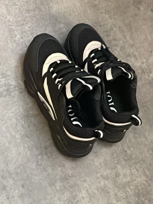 Dior B22 - Snygga chunky sneakers från Dior i svart och vitt. Skorna har en kraftig sula, meshdetaljer och vita kontrastpaneler. Klassisk snörning och logga på insidan. Perfekta för dig som gillar streetwear och vill sticka ut med en exklusiv look.
