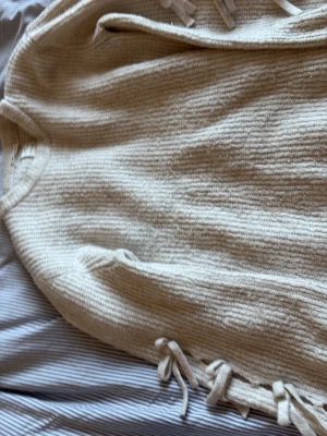 Beige stickad tröja från Zara - Mysig beige stickad tröja från Zara Knitwear, winter collection. Tröjan har rund halsringning och dekorativa knytband längs båda sidorna. Perfekt för kalla dagar och enkel att matcha med jeans eller kjol. Knappt använd dessutom! Funkar även för stl xs-s