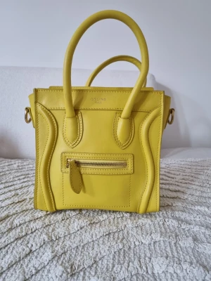 Gul Celine Nano Luggage handväska - Säljer en ikonisk gul Celine Nano Luggage handväska i slätt läder. Väskan har dubbla topphandtag, en liten dragkedjeficka framtill och detaljerade sömmar. Perfekt för dig som vill sticka ut med en färgglad och trendig accessoar.