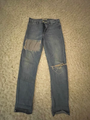 Blå patchade jeans från Acne Jeans - Säljer ett par blå jeans från Acne Jeans med raka ben och slitna detaljer. Längst nere på byxorna är det avklippt därav det låga priset. W26 L34