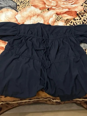 Mörkblå offshoulder blus med snörning - Trendig mörkblå offshoulder blus med snygga snörningsdetaljer framtill. Blusen har en avslappnad passform och långa ärmar med lätt puff. Perfekt att styla med jeans eller kjol för en cool look. Helt oanvänd. 