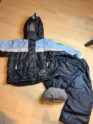 Svarta täckbyxor från Mywear - Säljer ett par svarta täckbyxor från Mywear i storlek 86/92. Materialet är slitstark polyester med mjukt fleecefoder på insidan. Perfekta för kalla dagar och har resår i midjan för skön passform. Matchar med jacka i samma stil.