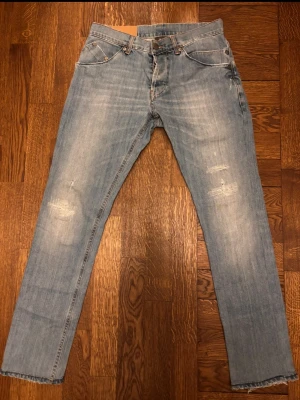 Ljusblå dondup jeans - Säljer ett par ljusblå jeans med raka ben och slitningar på låren och knäna. Jeansen har klassisk femficksmodell, normal midja och synliga sömmar. Perfekta för en avslappnad och trendig look. Tar emot prisförslag! Titta i profilen för fler liknande par!