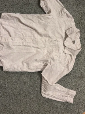 Beige skjorta från Lindex Kids - Stilren beige skjorta från Lindex Kids i storlek 158. Skjortan har klassisk krage, bröstficka och knäppning framtill. Tillverkad i ett mjukt material som känns skönt mot huden. Perfekt för dig som gillar en enkel och clean look.