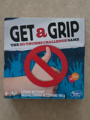 Get a Grip - The No Thumbs Challenge Game - Roligt sällskapsspel från Hasbro där du ska klara utmaningar utan att använda tummarna. Innehåller olika spelkort, utmaningar och tillbehör. Perfekt för spelkvällar med vänner eller familj. För 8 år och uppåt.
