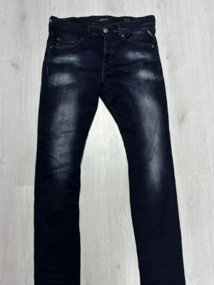 Mörkblå Replay jeans  - Snygga mörkblå jeans från Replay med coola slitningar och tvättade detaljer på låren och knäna. Klassisk femficksmodell med raka ben och broderade bakfickor. Perfekta för en avslappnad och trendig look.