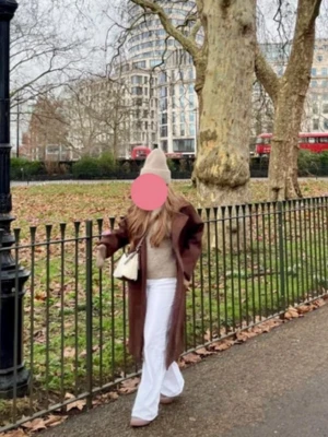 Brun lång ullkappa med bred krage - Snygg brun lång kappa med bred krage och dubbelknäppning. Kappan har en rak passform och är tillverkad i ett ull-liknande material som håller dig varm. Perfekt för kyliga dagar och ger en stilren look.