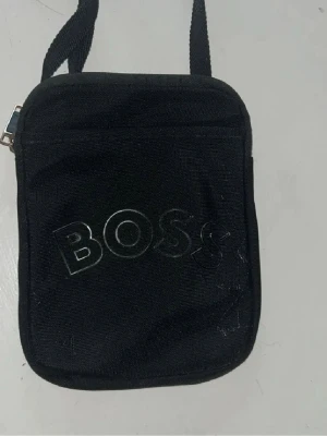 Svart axelväska från BOSS - Snygg svart axelväska från BOSS med justerbar axelrem och dragkedja. Säljer den eftersom jag ändrat stil helt enkelt. Perfekt för som gillar märkes kläder