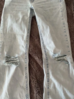 Ljusblå slitna jeans med hål - Säljer ett par ljusblå jeans bootcut och slitna detaljer över knäna. Jeansen har en klassisk femficksmodell och är tillverkade i denim. Perfekta för en avslappnad och trendig look. Endast andvänd 1 gång säljer då dom inte kommer till andvändning 