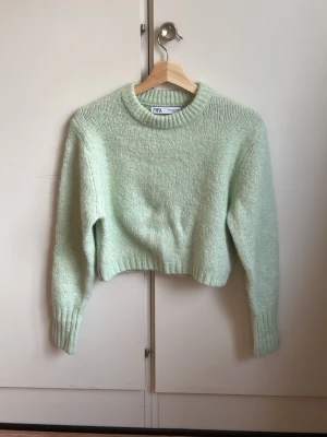 Mintgrön cropped stickad tröja Zara - Säljer en mintgrön stickad tröja från Zara med croppad passform och rund hals. Tröjan har långa ärmar och ribbade muddar vid ärmslut och nederkant. Perfekt för dig som gillar en fräsch och trendig look.