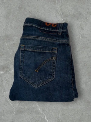 Dondup George  - Snygga mörkblå jeans från dondup med slim fit  och klassisk femficksdesign. Jeansen har kontrastsömmar och en diskret dondup logga på bakfickan. Tillverkade i slitstark denim som passar perfekt till en avslappnad stil. Modell: George