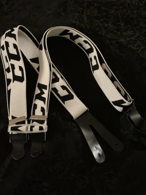 Svarta och vita hängslen från CCM - Säljer ett par stilrena hängslen från CCM i svart och vitt med tydlig logga längs banden. Hängslena har breda elastiska band och detaljer i svart konstläder för fäste. Perfekt accessoar för dig som vill sticka ut lite extra.