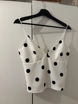 Vit prickig linnetopp med tunna band - Snygg vit linnetopp med svarta prickar och tunna axelband.  Storlek L men rätt kort. Passar minder storlek då den är liten i storleken. Helt ny aldrig använd då den var kortare än vad jag trodde.