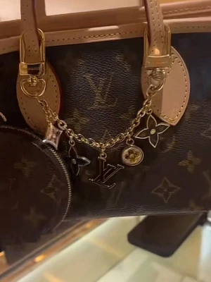 Louis Vuitton guldigt charmarmband - Snyggt bag charm från Louis Vuitton i guldfärgad metall med ikoniska LV-berlocker och blommor i svart, vitt och guld.