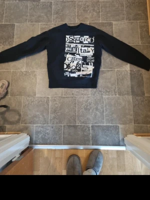 Svart Dsquared2 sweatshirt med tryck - Cool svart sweatshirt från Dsquared2 med stort vitt grafiskt tryck framtill. Tröjan har rund halsringning och långa ärmar. Perfekt för dig som gillar streetwear och vill sticka ut med en unik design.