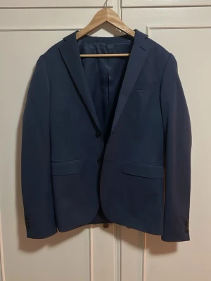 Mörkblå klassisk kavaj från Bläck - Säljer en kavaj från Bläck som är använd endast ett fåtal gånger. Osäker på exakt storlek men den sitter ungefär som en M eller 50.