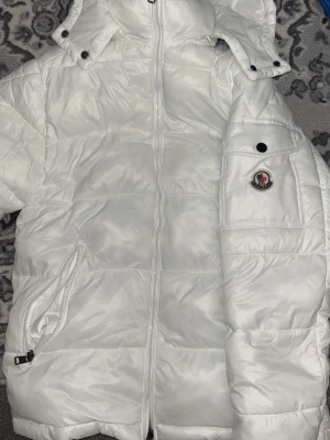 Vit dunjacka från Moncler - OBS pris kan diskuteras!!!!Snygg vit dunjacka från Moncler med huva och dragkedja framtill. Jackan har en ficka med knapp och Moncler-logga på ärmen samt snedställda fickor med dragkedja. Perfekt för kalla vinterdagar och riktigt trendig look.