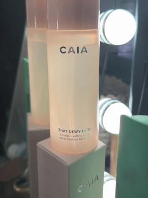 CAIA That Dewy Look  - Setting spray  från CAIA i modellen That Dewy Look. Kommer i en stilren, cylinderformad flaska i ljusrosa plast med vit text. Ger en glowig finish och funkar perfekt för att fixera sminket och återfukta huden under dagen. På bild två syns det att den är typ full jag har sprayat 2-3 gånger bara.
