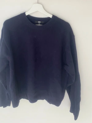 Mörkblå stickad tröja från Uniqlo - En enkel och stilren mörkblå stickad tröja från Uniqlo med rund halsringning och ribbade muddar vid ärmslut och nederkant. Perfekt för lager på lager och passar till det mesta i garderoben.