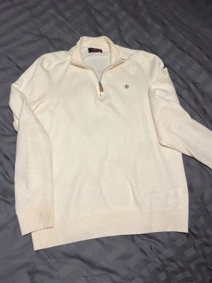 Moris  - Snygg vit tröja från Schott NYC med halvzip och ribbade muddar. Tröjan har en liten broderad logga på bröstet och är tillverkad i mjukt material. Perfekt för lager-på-lager och enkel att matcha med olika outfits.