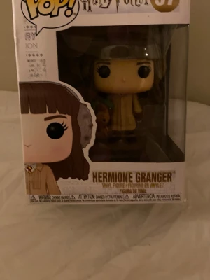 Funko Pop Hermione Granger figur - Säljer en Funko Pop vinylfigur av Hermione Granger från Harry Potter. Figuren är brunhårig och har på sig öronmuffar och en beige tröja. Kommer i originalförpackning med fönster så man ser figuren tydligt.