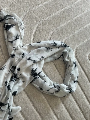 Vit sjal med svart mönster - Säljer en tunn och luftig vit sjal med svart abstrakt mönster. Sjalen är rektangulär och tillverkad i ett lätt och mjukt material som känns skönt mot huden. Perfekt att slänga över axlarna för en cool och stilren look.