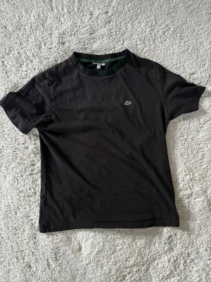 Lacoste t shirt - Svart t-shirt från Lacoste med klassisk rund hals och det ikoniska gröna krokodilmärket broderat på bröstet. Storleken är 16 men passar S. Den är lite använd. Hör av dej vid intresse