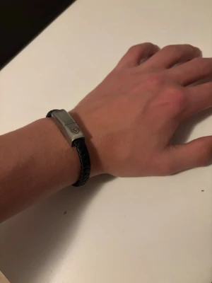 Svart flätat armband med iPhone laddare - Stilrent svart armband med flätad design, det är en iPhone laddare inbyggt vilket gör att den är perfekt att ha på sig i vardagen då du alltid har en laddare på dig samtidigt som den är grymt stilren