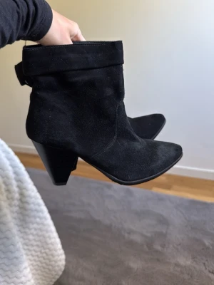 Svarta boots i mocka med klack - Snygga svarta stövletter i mocka med bred, konformad klack och spetsig tå. Skaftet är något slouchy och kan vikas ner för en cool look. Perfekta till jeans eller kjol för en trendig outfit. Aldrig använda