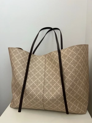 By Malene beiger  - Säljer en stor malene briger väska i modellen ”Abi tote bag” i färgen incense. Modellen finns inte längre att köpa vilket gör väskan mer exklusiv och svårare att få tag på, säljer den då den inte kommer till anvädning. Väskan är perfekt om man vill få i mycket. Väskan har i sig inga defekter förutom en liten fläck inuti, som man ser på sista bilden. Nypris på väskan är 3500. Dustbag medföljer skriv vid funderingar !!💕måtten på väskan: 35cm x 55cm x 16cm