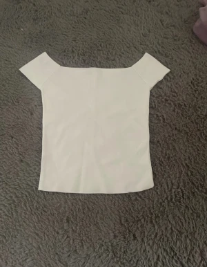 Vit offshoulder topp - Snygg vit offshoulder topp med korta ärmar och rak passform. Toppens material känns stretchigt och mjukt, perfekt för en stilren look. Enkel design utan mönster eller detaljer, vilket gör den lätt att matcha med olika outfits.