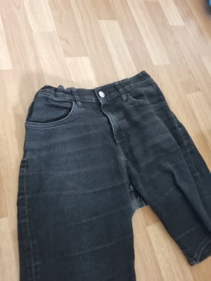 Svarta raka jeans med hög midja - Säljer ett par svarta jeans med rak passform och hög midja. Jeansen har klassiska fem fickor, bälteshällor och stängs med knapp och dragkedja. Materialet är denim i bomull och de har en snygg tvättad look.