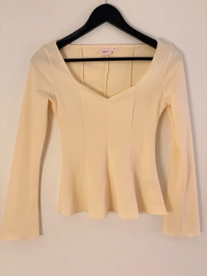 ljus gul långärmad topp från Gina Tricot - Superfin beige topp från Gina Tricot med lång ärm och v-ringad hals. Figurnära passform med lätt utsvängd nederkant. Perfekt att styla med jeans eller kjol för en clean look.