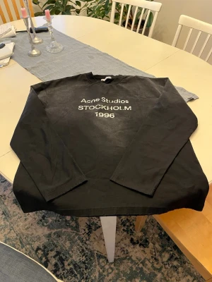 Svart Acne Studios storlek M - Acne Studios long sleeves i storlek M. Tvättad vintage look med vit “Acne Studios Stockholm 1996” text framtill. Mjukt material och relaxed/oversized fit som passar perfekt till en clean streetwear outfit.  • Storlek: M • Passform: Unisex • Skick: ny skick