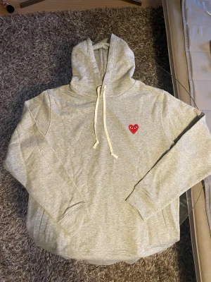 Grå hoodie från Comme des Garçons Play - Riktigt skön träna från Amo, den är storlek xl men kanske lite stor i storleken. Sjukt skön nu till vår dagarna då den är lite tun men samtidigt varm. Sitter snyggt, knappast använd pris kan diskuteras! 