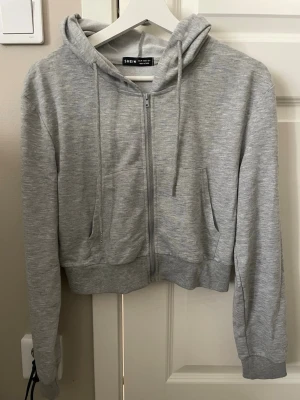 Grå kort zip hoodie - Ljusgrå hoodie från SHEIN med dragkedja framtill, huva med dragsnören och två fickor. Tillverkad i mjukt sweatshirtmaterial som är perfekt för chill dagar. Klassisk passform och ribbade muddar vid ärmar och nederkant. En magtröja