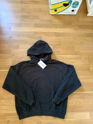 Svart hoodie från Acne Studios - Snygg svart hoodie från Acne Studios med klassisk passform och huva. Tillverkad i mjuk bomull som känns skön mot huden. Perfekt för en avslappnad och stilren look. Diskret logga på insidan av kragen och ribbade muddar vid ärmslut och nederkant.