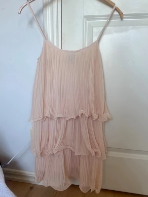 Plisserad Volangklänning från HM - Superfin ljusrosa/beige klänning med tunna axelband och volanger. Klänningen är plisserad och passar perfekt till sommaren. Väldigt eftertraktad klänning som tyvärr inte säljs längre! Den är