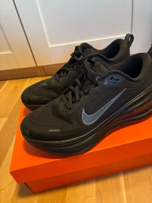 Svarta Nike Zoom sneakers -  Säljer sonens endast provade en gång !  Snygga svarta Nike Zoom sneakers med grå swoosh på sidan och texten 'Vomeric Fly' på plösen. Ovandel i mesh för bra andningsförmåga och bekväm passform. Tjock sula för extra dämpning och sportig look. Perfekta för dig som gillar stilrena och sportiga skor.