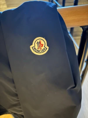 Mörkblå vindjacka från Moncler - Snygg mörkblå vindjacka från Moncler med klassisk logotyp på ärmen.Väldigt clean och stilren modell som passar till allt. Jackan är i fint skick och används tyvärr för lite, därför säljer jag den. Perfekt som lättare jacka till vår, sommar och höst. Pris kan diskuteras vid snabb affär. Storlek S-M| köpt för 2500kr|