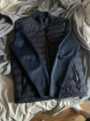 Mörkblå cardigan från Moncler - Snygg mörkblå cardigan från Moncler med quiltad front och släta ärmhål. Västen har dragkedja framtill, två dragkedjefickor och en diskret Moncler-logga på axeln. Perfekt för lager-på-lager och stilren look. Den är inte i den bästa skicken men de är bara att höra av sig om de. storlek 2=S