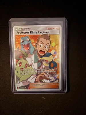 Pokémonkort Professor Elm's Lecture - Säljer ett samlarkort från Pokémon-serien, Professor Elm's Lecture. Kortet har färgglad design med flera Pokémon och text på engelska. Levereras i ett genomskinligt plastfodral för extra skydd. Perfekt för samlare eller Pokémon-fans.